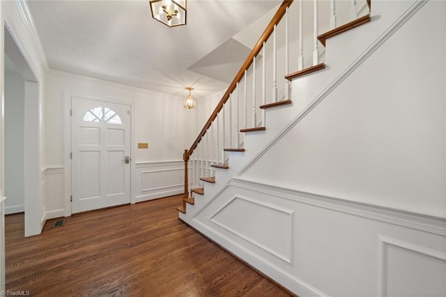 foyer entrance with an inviting chandelier, ornamental molding, and dark hardwood / wood-style flooring