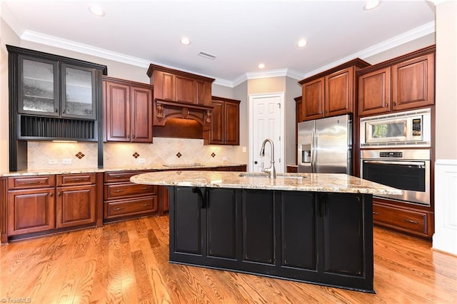 kitchen with stainless steel appliances, sink, light hardwood / wood-style floors, and a kitchen island with sink