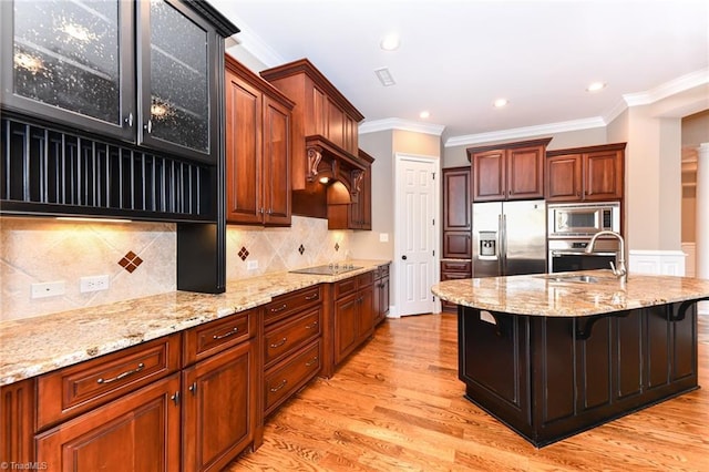 kitchen with sink, a kitchen island with sink, appliances with stainless steel finishes, a kitchen breakfast bar, and light stone counters