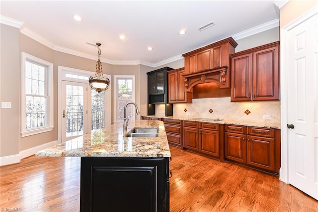 kitchen featuring backsplash, sink, ornamental molding, and a center island with sink