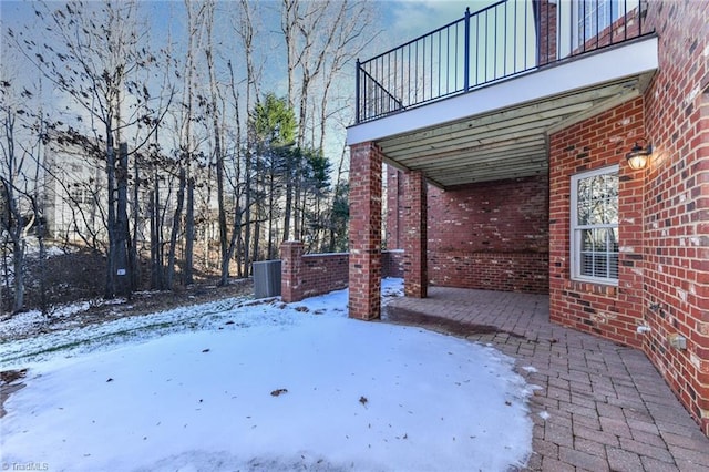 snowy yard featuring a balcony and central AC unit