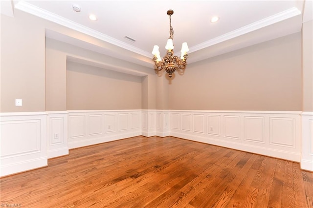 empty room with wood-type flooring, an inviting chandelier, and ornamental molding