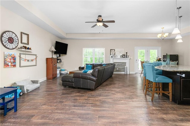 living room featuring dark wood-style flooring, baseboards, a wealth of natural light, and ceiling fan with notable chandelier