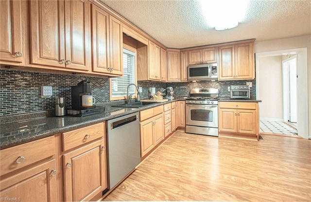 kitchen with sink, stainless steel appliances, light hardwood / wood-style flooring, backsplash, and dark stone counters