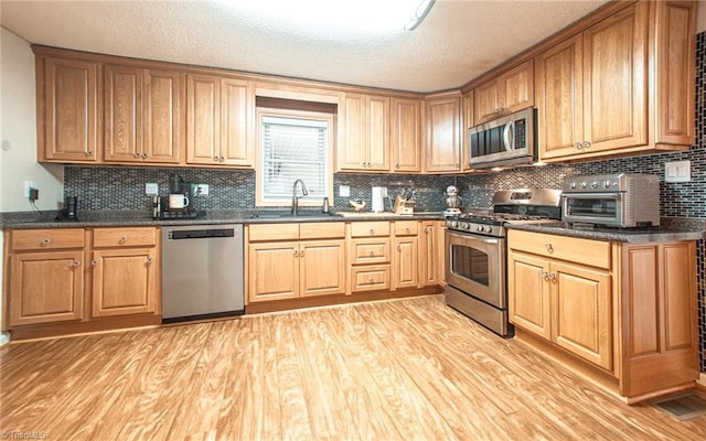 kitchen featuring sink, dark stone counters, a textured ceiling, appliances with stainless steel finishes, and light wood-type flooring