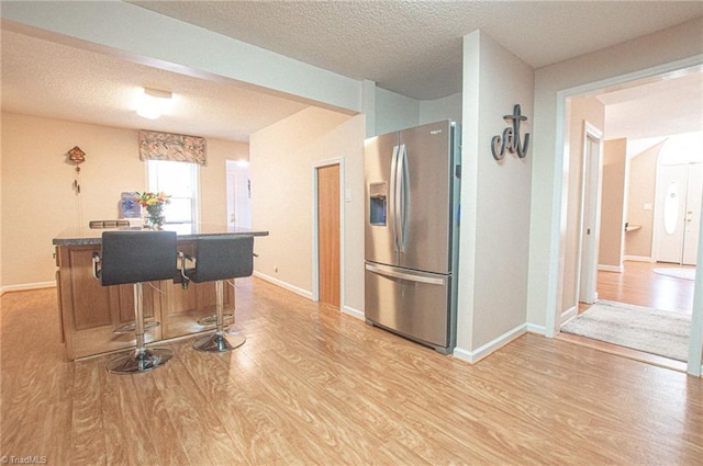 kitchen featuring a textured ceiling, a breakfast bar, light hardwood / wood-style floors, and stainless steel refrigerator with ice dispenser