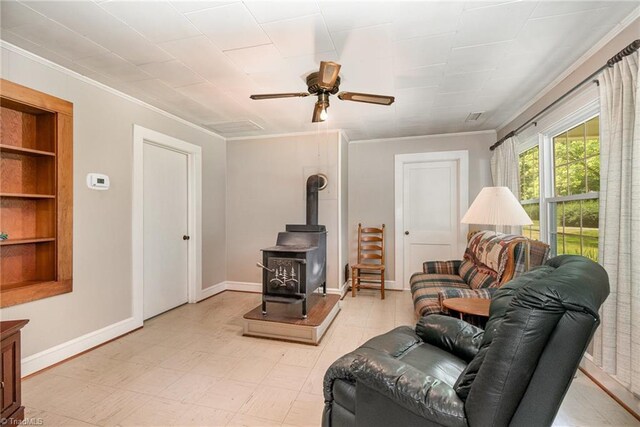 living room featuring crown molding, a wood stove, ceiling fan, and baseboards