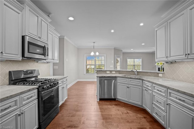 kitchen featuring ornamental molding, stainless steel appliances, sink, wood-type flooring, and a notable chandelier