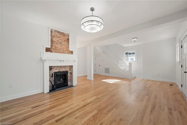 unfurnished living room with a brick fireplace and light hardwood / wood-style flooring