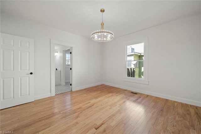 empty room featuring a notable chandelier, a healthy amount of sunlight, and light hardwood / wood-style floors