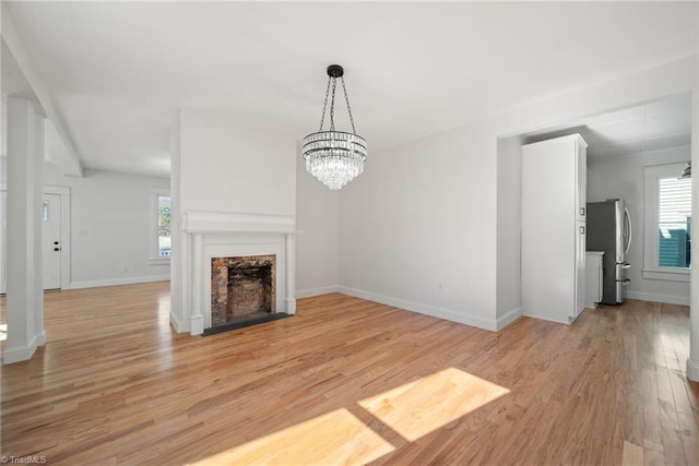 unfurnished living room featuring a notable chandelier, a wealth of natural light, and light hardwood / wood-style flooring