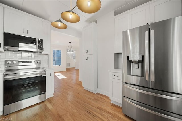 kitchen featuring white cabinets, hanging light fixtures, stainless steel appliances, and light wood-type flooring