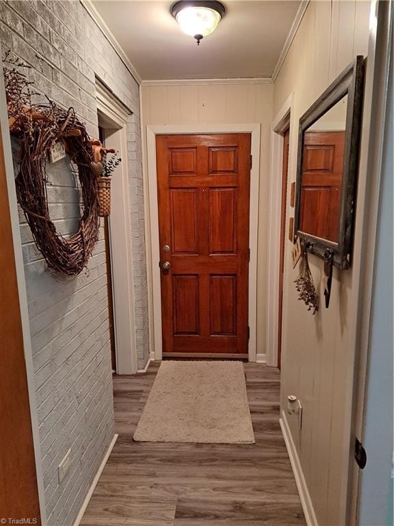 doorway with crown molding, hardwood / wood-style floors, and brick wall