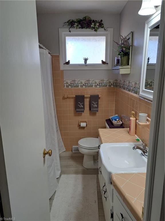 bathroom with vanity, toilet, tile walls, and walk in shower