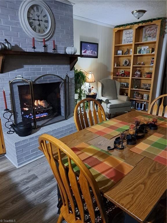 dining area featuring hardwood / wood-style floors, a textured ceiling, a brick fireplace, and crown molding