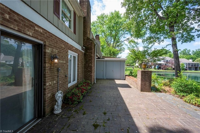 view of home's exterior with brick siding, a water view, a patio, and a chimney