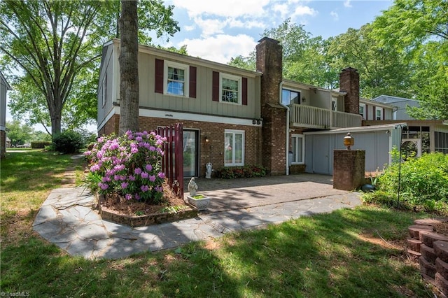 view of front of house with board and batten siding, brick siding, a chimney, and a front lawn