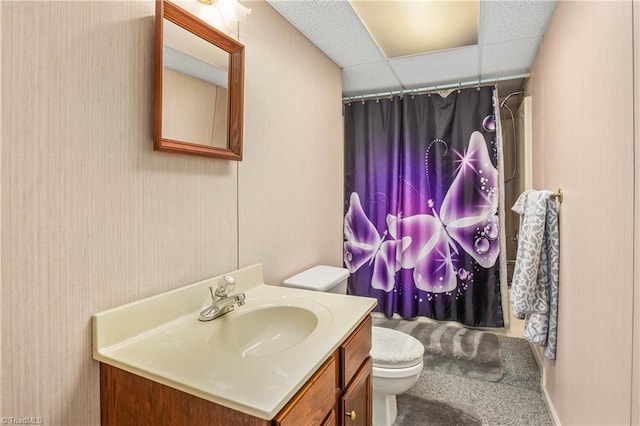 bathroom with walk in shower, a drop ceiling, vanity, and toilet