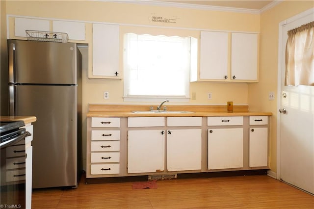 kitchen featuring sink, light hardwood / wood-style flooring, ornamental molding, white cabinetry, and stainless steel refrigerator