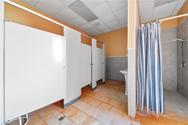 bathroom featuring tile patterned floors, a drop ceiling, and tile walls