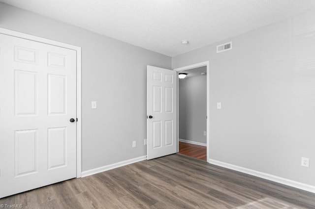 unfurnished bedroom featuring a closet, dark hardwood / wood-style floors, and a textured ceiling