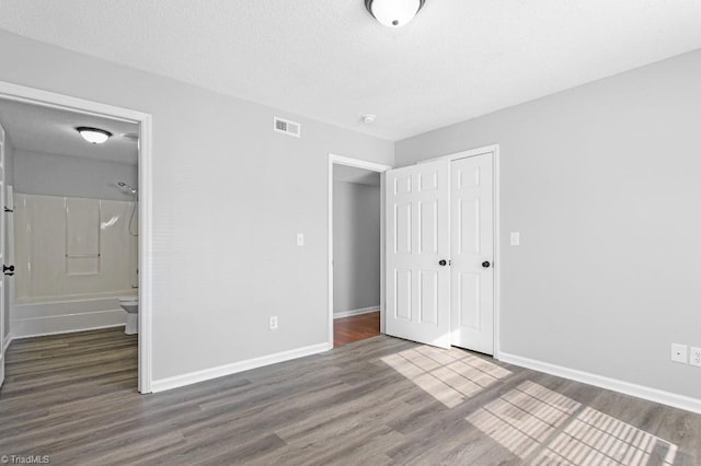 unfurnished bedroom with dark wood-type flooring, ensuite bathroom, and a closet