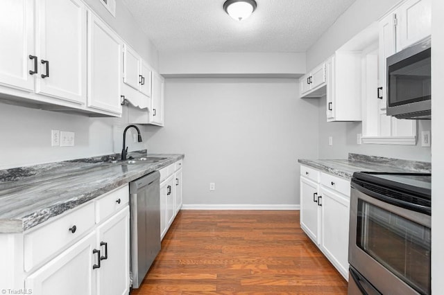 kitchen with a textured ceiling, dark stone counters, stainless steel appliances, and white cabinetry