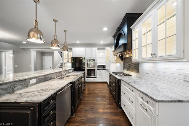 kitchen with pendant lighting, sink, stainless steel appliances, white cabinets, and a large island with sink