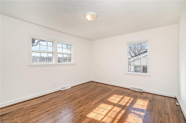 empty room with plenty of natural light, dark hardwood / wood-style floors, and a textured ceiling