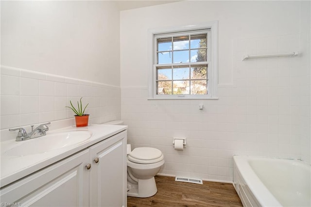 bathroom with vanity, hardwood / wood-style flooring, a washtub, toilet, and tile walls