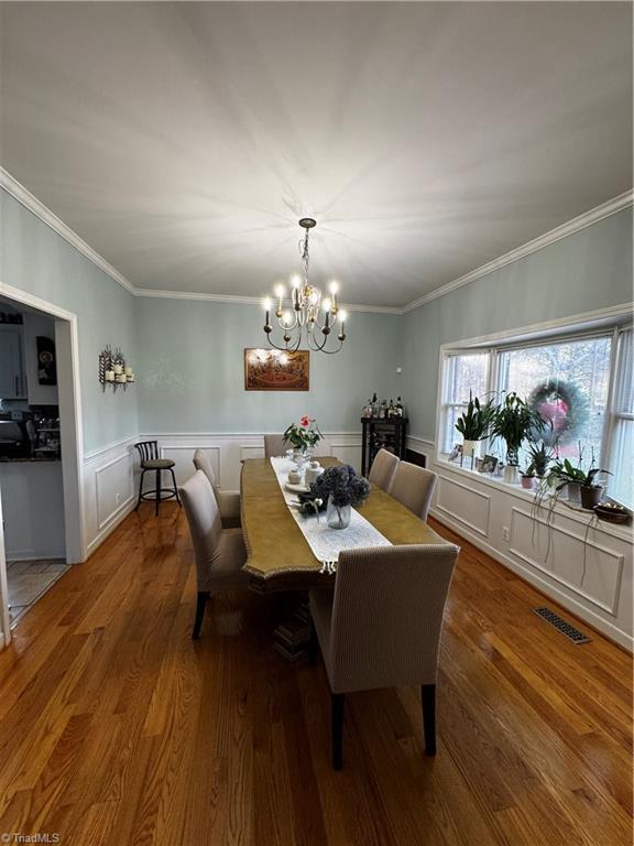 dining room with dark wood-style floors, crown molding, visible vents, an inviting chandelier, and wainscoting