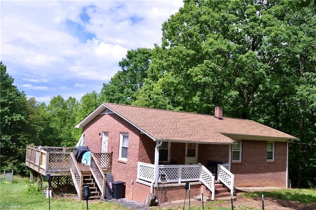 back of property featuring a porch, brick siding, stairway, a chimney, and roof with shingles