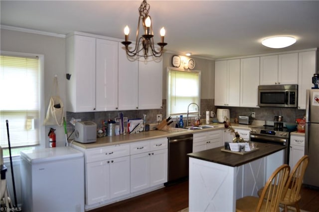 kitchen with appliances with stainless steel finishes, a sink, white cabinets, a chandelier, and decorative backsplash
