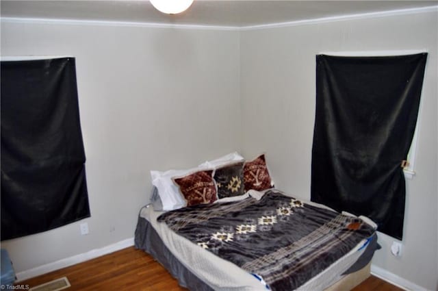 bedroom with ornamental molding, wood finished floors, and baseboards