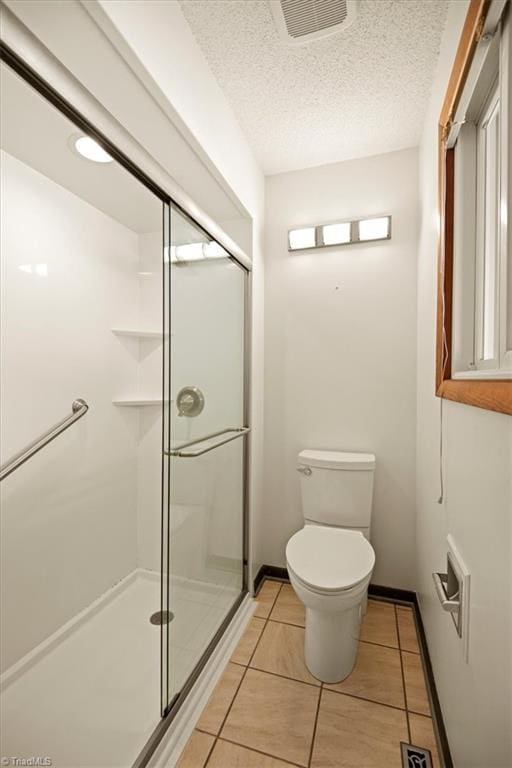 bathroom featuring toilet, tile patterned flooring, a textured ceiling, and a shower with door