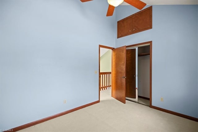 unfurnished bedroom with ceiling fan, a high ceiling, a closet, and light carpet