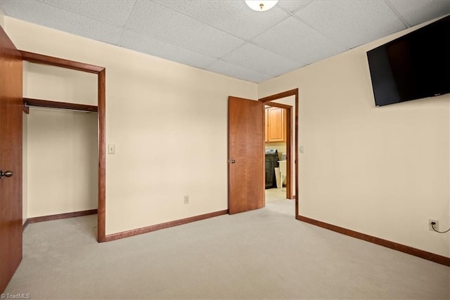 unfurnished bedroom with light colored carpet, a closet, and a paneled ceiling