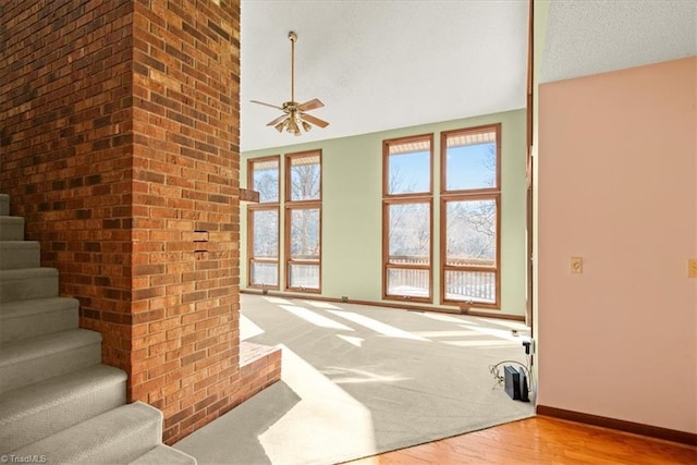 unfurnished living room with ceiling fan, light hardwood / wood-style floors, a textured ceiling, and high vaulted ceiling