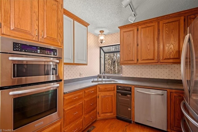 kitchen with track lighting, sink, stainless steel appliances, and light hardwood / wood-style flooring