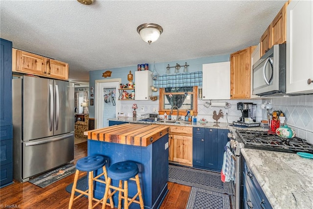 kitchen with butcher block counters, a breakfast bar area, dark wood-style floors, stainless steel appliances, and a sink