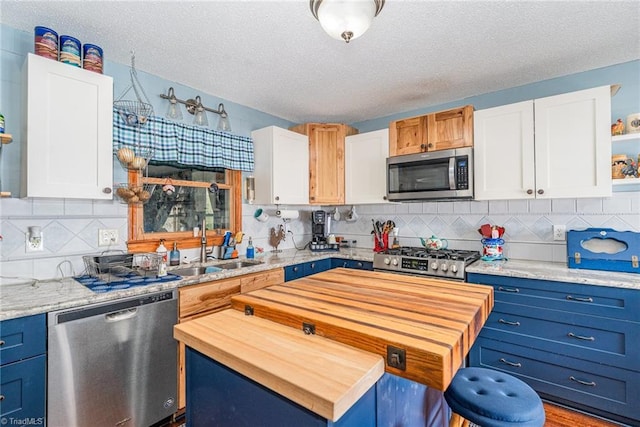 kitchen with a sink, a kitchen island, white cabinetry, appliances with stainless steel finishes, and wooden counters