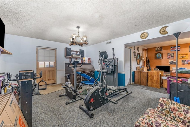 exercise room featuring visible vents, carpet floors, wood walls, a textured ceiling, and a notable chandelier