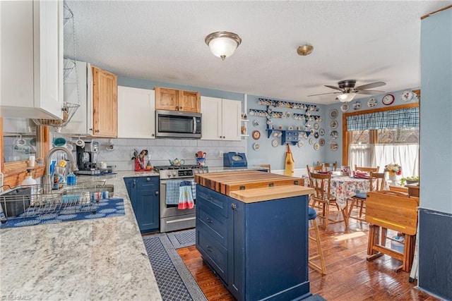 kitchen with a kitchen island, blue cabinetry, dark wood-style flooring, ceiling fan, and appliances with stainless steel finishes