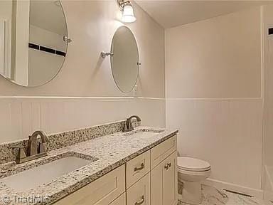 full bath featuring a sink, toilet, double vanity, and marble finish floor