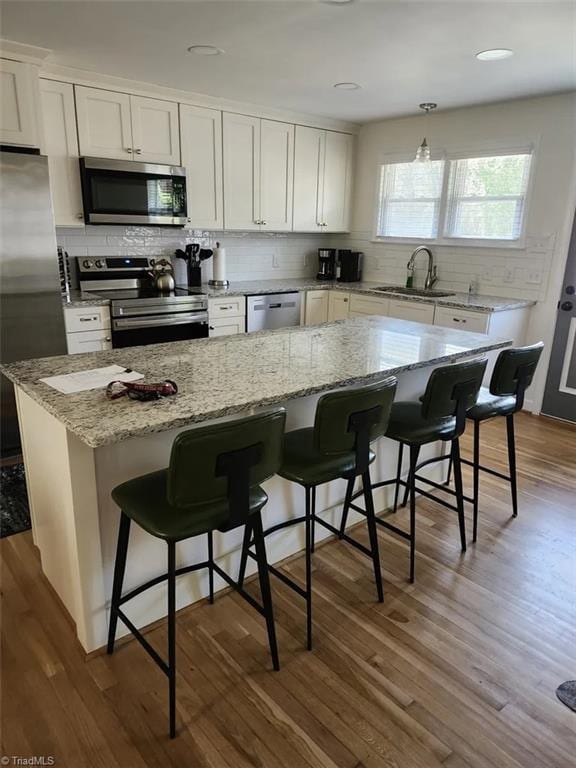 kitchen with tasteful backsplash, light stone countertops, a sink, white cabinets, and stainless steel appliances