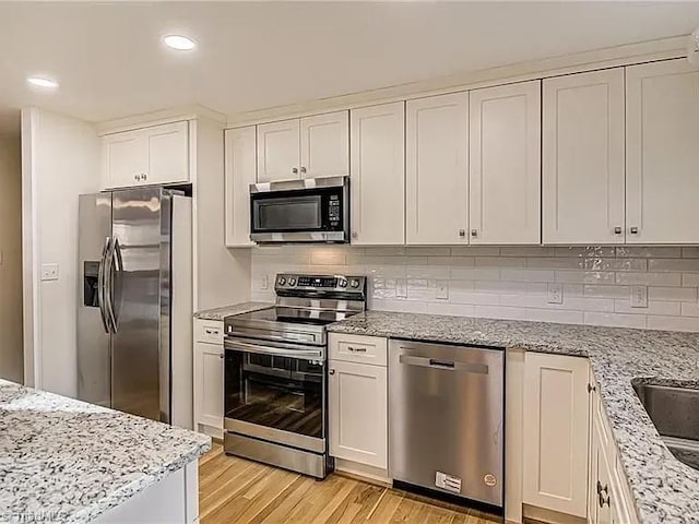 kitchen with light wood-type flooring, recessed lighting, white cabinetry, tasteful backsplash, and appliances with stainless steel finishes