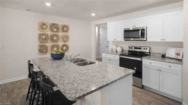 kitchen featuring light stone counters, a sink, a center island with sink, appliances with stainless steel finishes, and white cabinetry