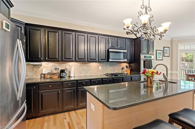 kitchen featuring stainless steel appliances, a sink, a chandelier, ornamental molding, and tasteful backsplash