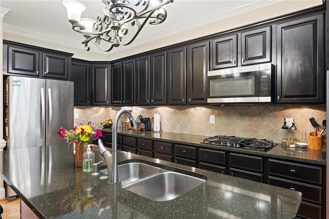 kitchen featuring appliances with stainless steel finishes, a sink, a chandelier, dark cabinets, and dark stone countertops