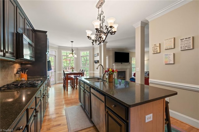 kitchen with a sink, stainless steel microwave, a chandelier, light wood-style flooring, and ornamental molding